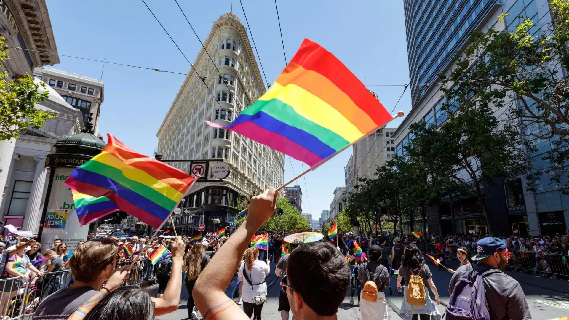 People walking in the 贝博体彩app骄傲节 parade wave rainbow flags.