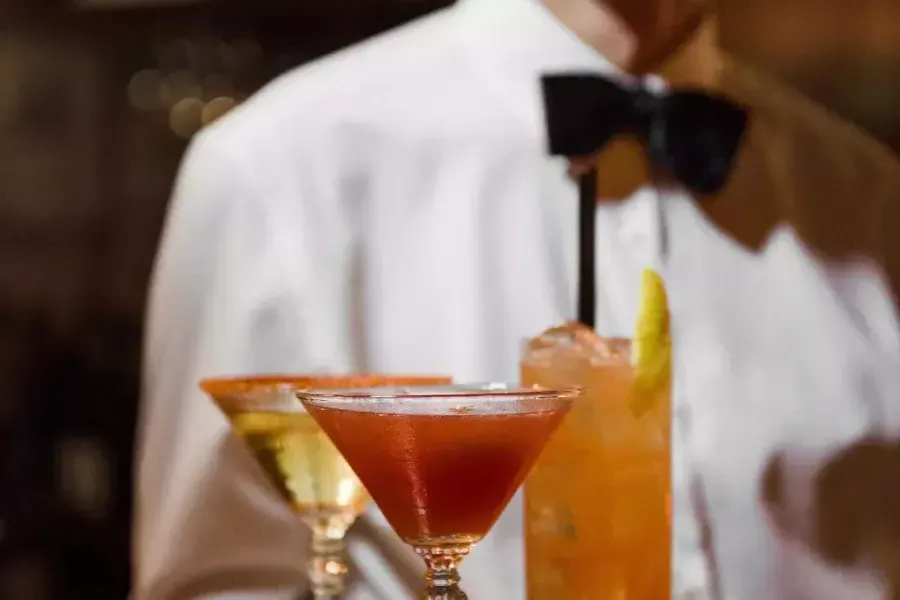 A server wearing a bowtie presents a tray of cocktails at Absinthe Restaurant 在贝博体彩app.