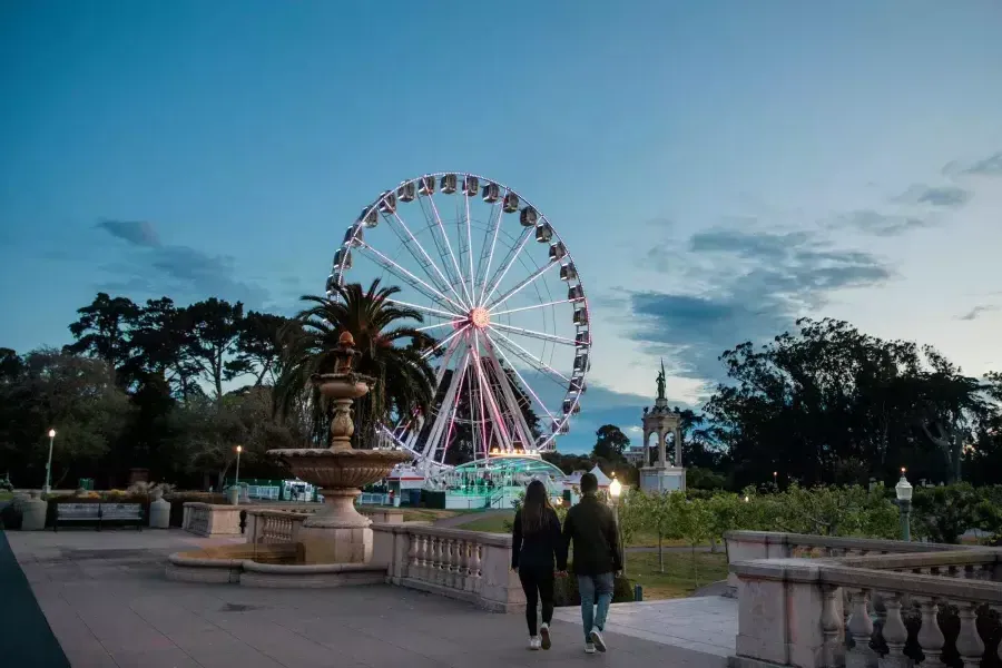 Una pareja camina hacia la noria SkyStar al anochecer.