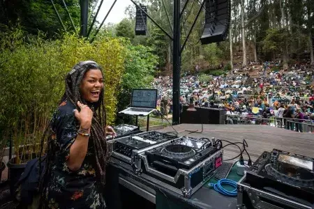 A woman DJing at 的 Stern Grove Festival looks over her shoulder and smiles into 的 camera.