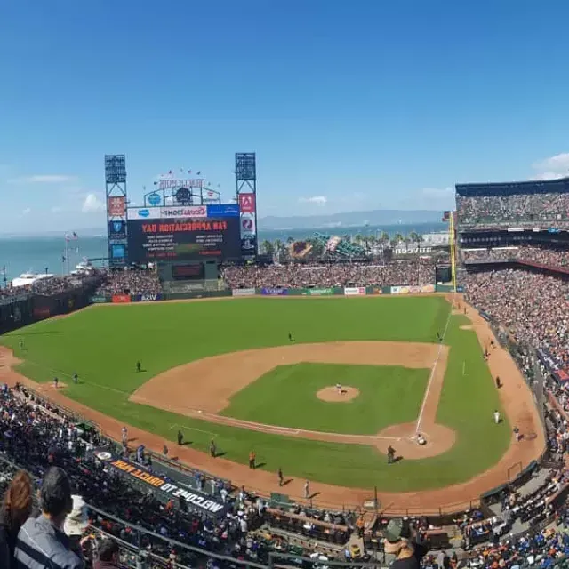 Uma vista do Oracle Park de São Francisco olhando das arquibancadas, 和 o campo de beisebol em primeiro plano e a Baía de São Francisco ao fundo.